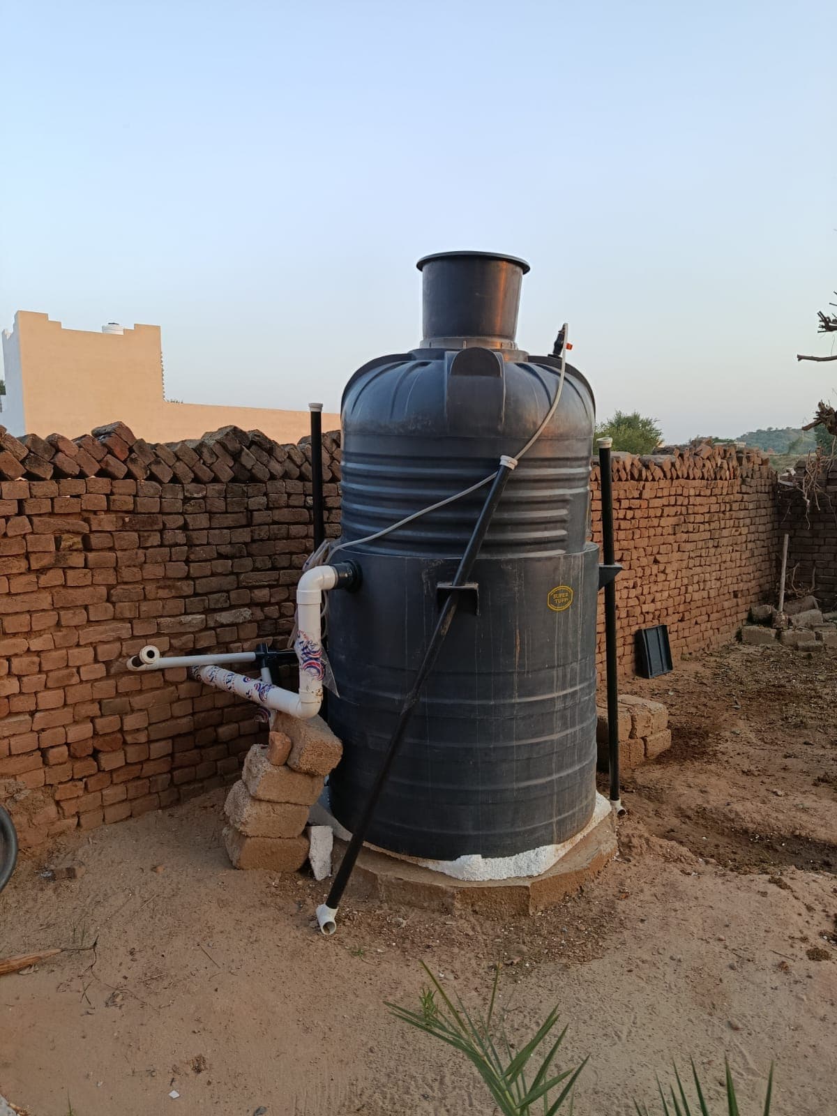 A ZES digester installed beside a brick boundary wall, gas line running from the dome