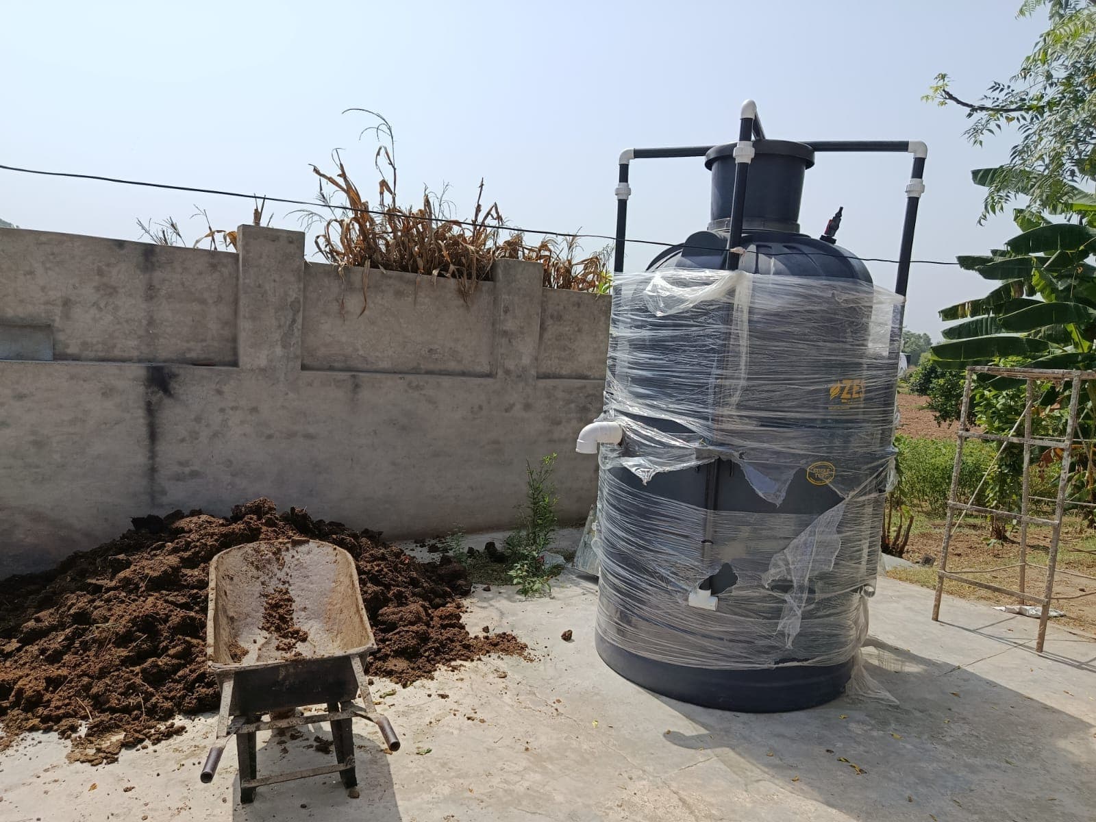 An installed digester with a barrow of dung alongside it, ready for the daily feed